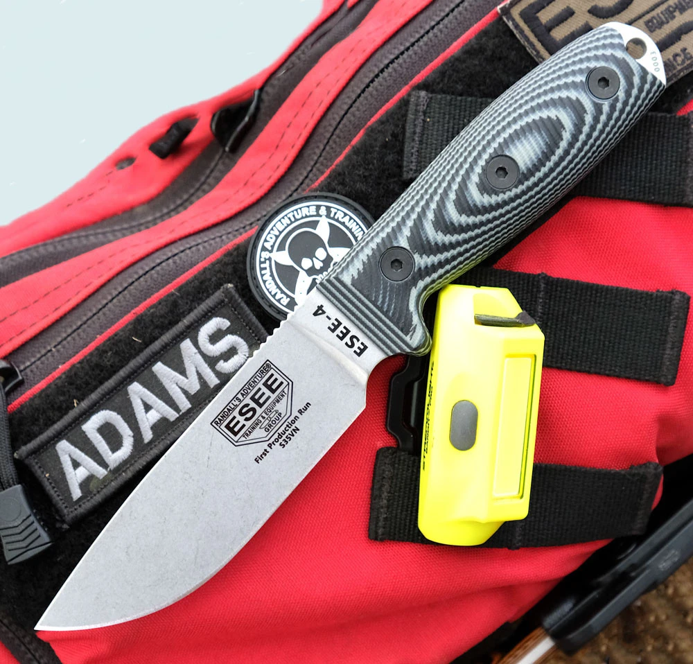 The ESEE-4 3D Handle (ESEE-4S35V) shown with its 4.50-inch CPM-S35VN drop point blade in a stonewash finish and flat grind, 3D gray and black G-10 handle scales, and its injection-molded black polymer sheath.