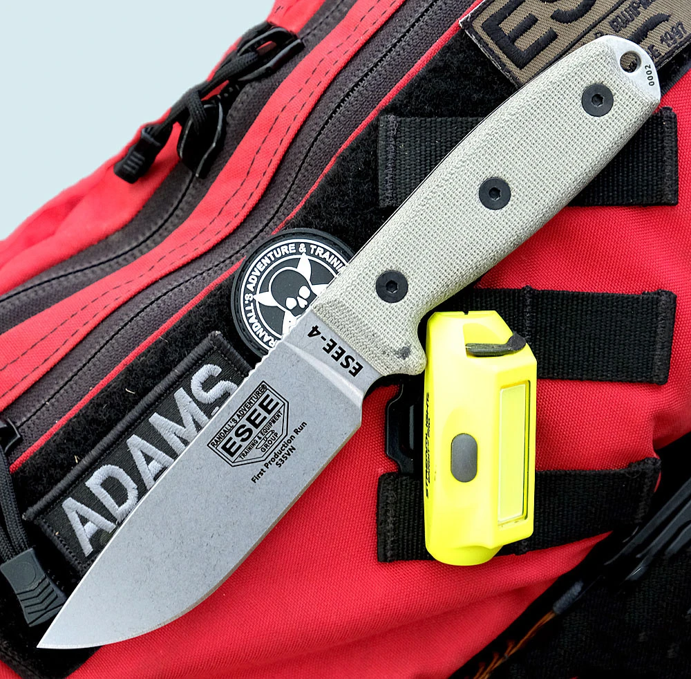 The ESEE-4 (ESEE-4P35V) shown with its 4.5-inch CPM-S35VN drop point blade in a stonewash finish and flat grind, tan Micarta handle scales, and its injection-molded black polymer sheath.