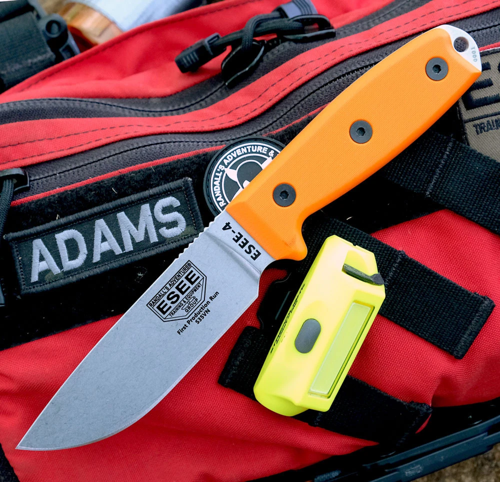 The ESEE-4 (ESEE-4P35V-OR) shown with its 4.5-inch CPM-S35VN drop point blade in a stonewash finish and flat grind, orange G-10 handle scales, and its injection-molded black polymer sheath.