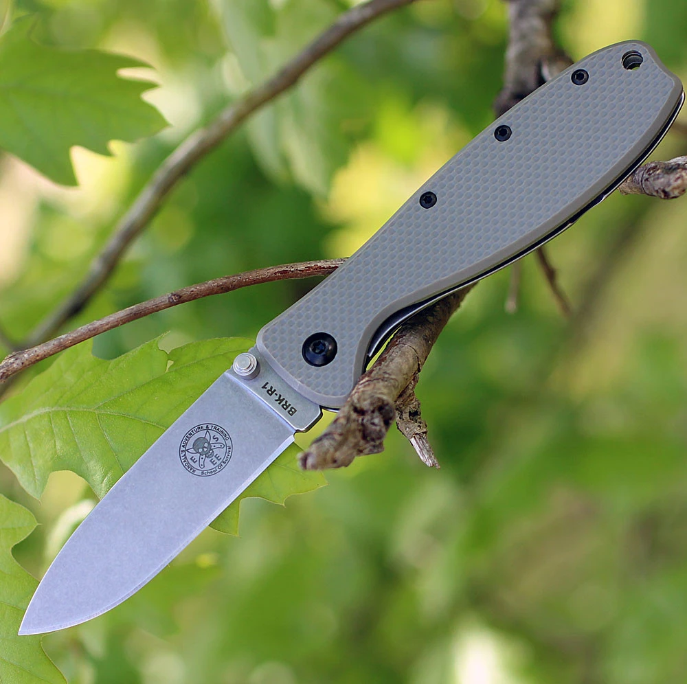 The ESEE Zancudo (BRKR1FG) shown with its 2.94-inch AUS-8 drop point blade in a stonewash finish and flat grind, Foliage Green polymer handle with steel frame lock, and reversible pocket clip for tip-up or tip-down carry.