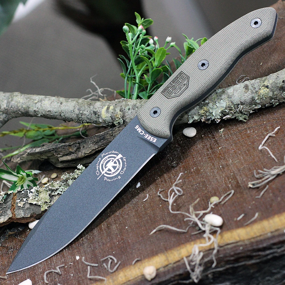 The ESEE-CM6 (ESEE-CM-6-TG) shown with its 5.88-inch 1095 clip point blade in a Tactical Gray finish and flat grind with a sharpened swedge, full-sized tan Micarta handle scales, and its black Kydex sheath with multiple carry options.