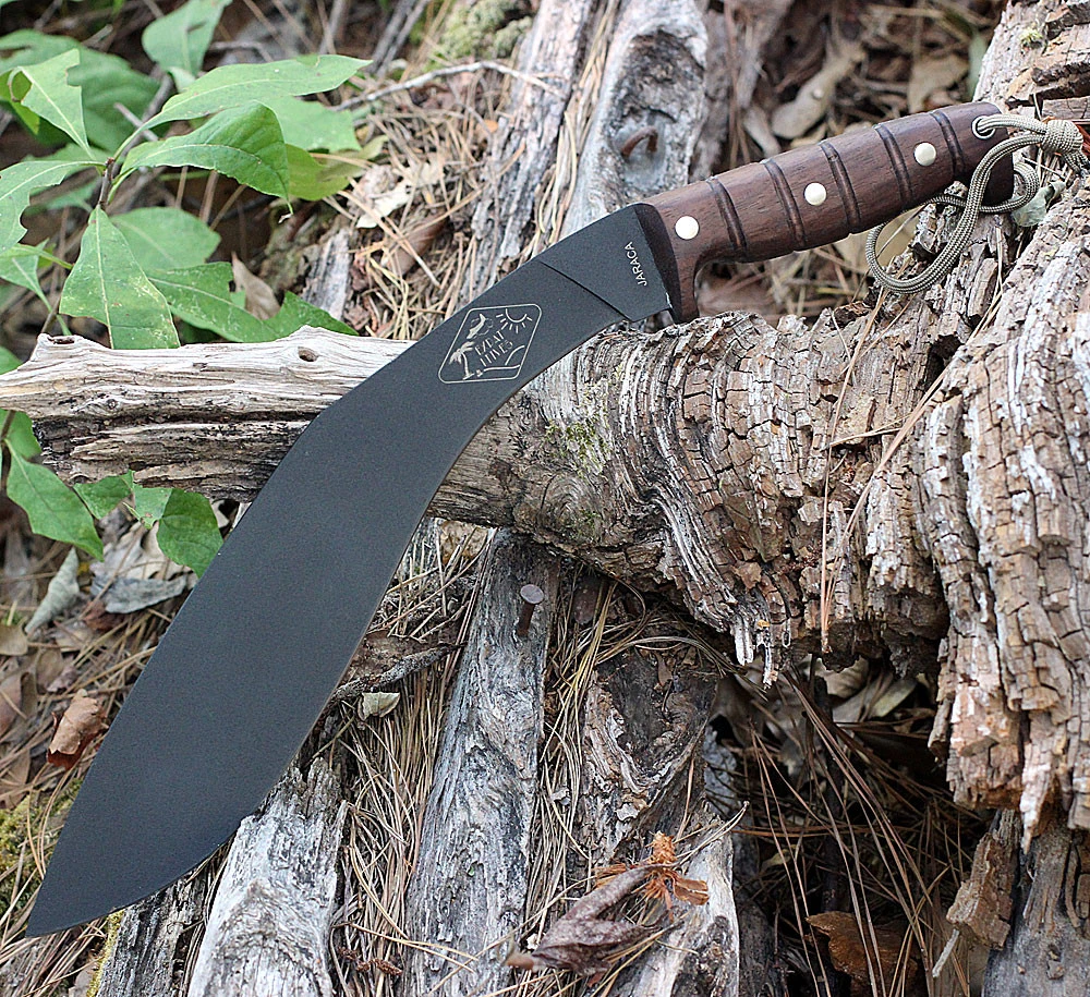 The ESEE Expat Jaraca Kukri (ESEE-KUKRI) shown with its 11.50-inch 1075 high carbon steel kukri blade in a black traction powder coating with flat grind and convex edge, walnut wood handle with forward and rear guards, and its khaki Cordura sheath.