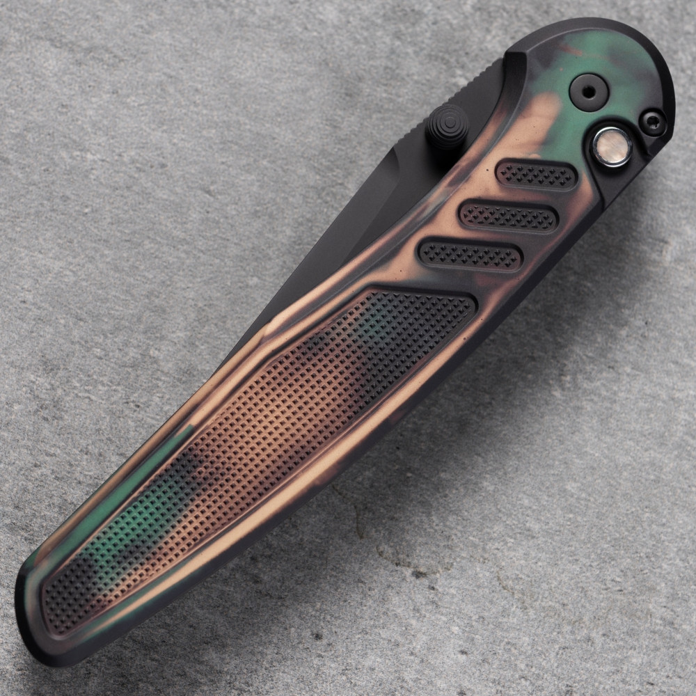 Close-up detail of the Pro-Tech Avalon PN1103-SHIPWRECK handle on a gray concrete surface, showing the Shipwreck cerakote finish in detail — copper, orange, and brown tones over the knurled aluminum scales. The black lip pearl button and black hardware are visible against the multicolor handle pattern.