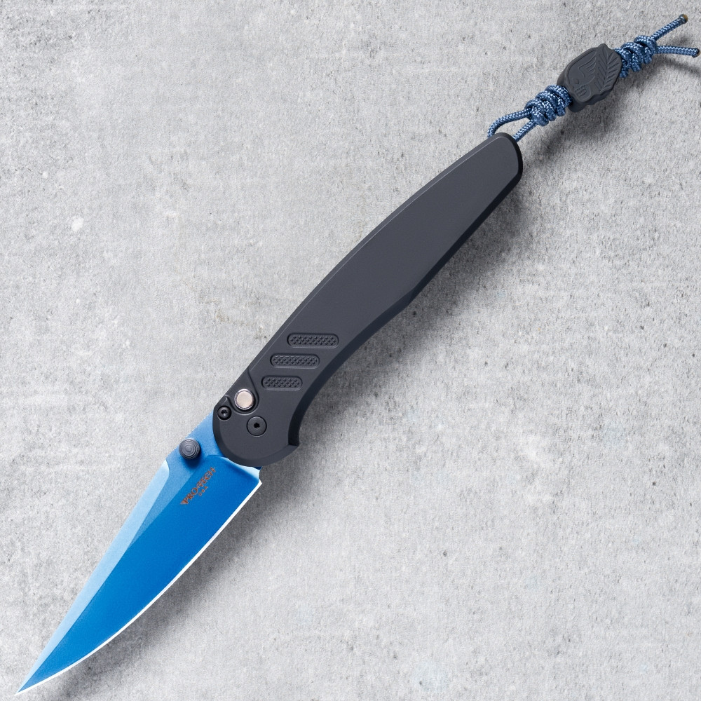 Pro-Tech Avalon BSA26.Avalon.1 shown open on a gray concrete surface with the sapphire blue PVD CPM MagnaCut drop point blade fully deployed. The vivid blue blade contrasts sharply against the solid black aluminum handle, with the lanyard visible at the base of the handle.