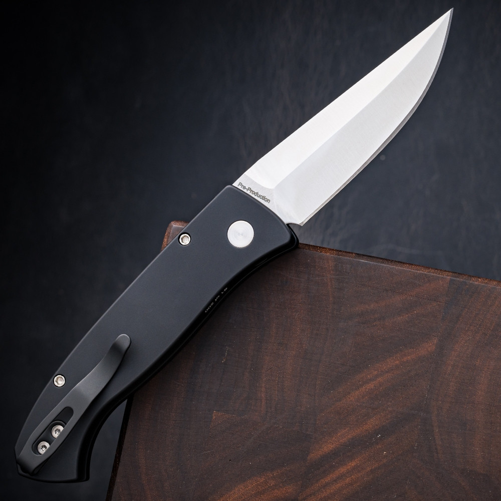 Pro-Tech Brend Classic BSA26.Brend.1 shown open against a dark walnut wood background, angled to display the full length of the knife from a slightly elevated perspective. The satin 154CM blade and solid black aluminum handle are both in frame, showing the overall proportions of the Brend 1 platform.