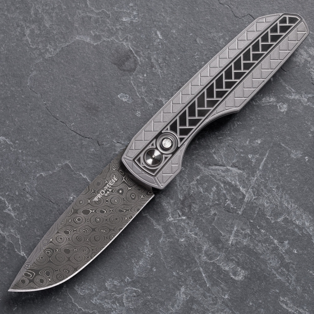 Pro-Tech VERO Synapse 2 Custom 002 shown open on a gray slate surface. The Chad Nichols Raindrop Damascus blade is fully deployed and the full profile of the knife is visible, with the 2-tone blasted and tumbled 17-4 herringbone textured steel handle and deployed Damascus blade both clearly in frame.