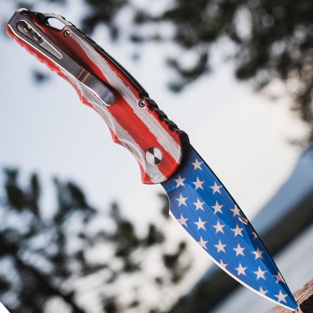 Pro-Tech TR-5 T501-PATRIOT shown against a blue sky background with the red and white stripes of the Patriot Cerakote blade finish as the focal element. The CPM-S35VN drop point blade and the continuity of the USA flag Cerakote from handle to blade are clearly visible in this profile shot.