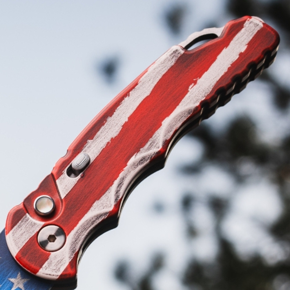 Pro-Tech TR-5 T501-PATRIOT shown in a closed or angled position against a blue sky background. The full red, white, and blue USA flag Patriot Cerakote finish covering the aluminum handle and blade, the deep-carry pocket clip, and the slide safety are visible from this perspective.