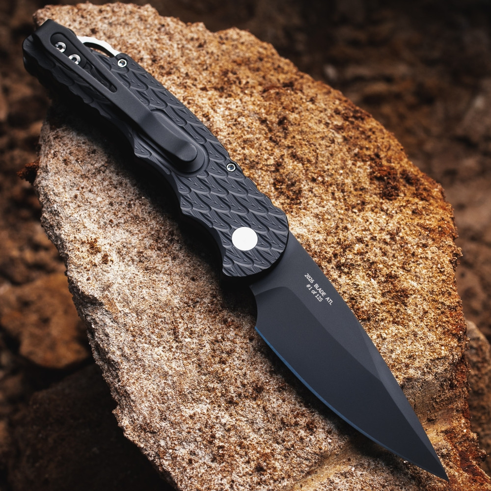 Pro-Tech TR-5 BSA26.TR5.1 shown at an angled profile on a rough stone surface. The feather-textured black aluminum handle, integrated steel glass breaker, black deep-carry pocket clip, and DLC black blade tip are all visible from this perspective, showing the full-feature TR-5 platform in the BSA26 configuration.
