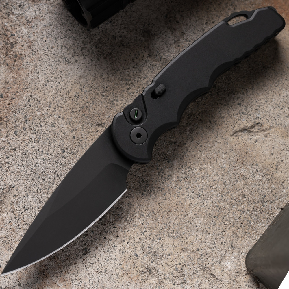 Pro-Tech TR-5 Operator T503-Operator shown open on a sandy concrete surface. The fully sterile DLC black CPM-S35VN drop point blade is deployed with no markings or engravings visible on the blade or handle. The all-black build and tritium push button are visible from this side profile angle.
