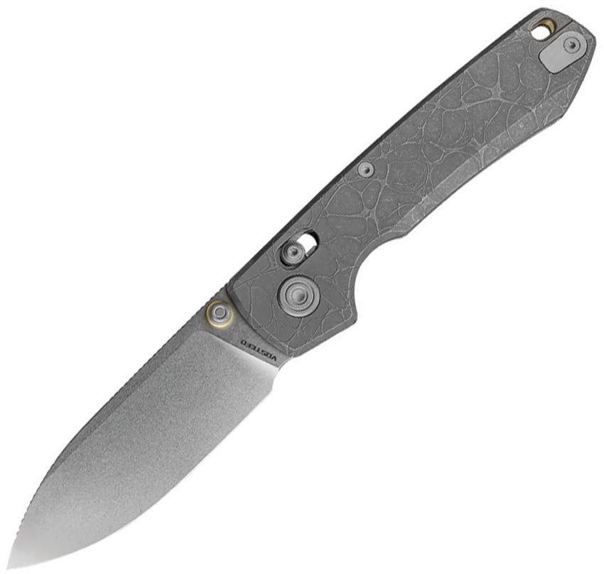 The Vosteed Raccoon TiSlim (A4506) is shown diagonally against a white background in the closed position, spine facing up. The stonewash gray CPM-S35VN drop point blade extends to the left. The full titanium handle displays acid wash gray finish with a distinctive crackle-cell pattern texture. Gold-toned hardware is visible at the pivot. The crossbar lock mechanism, a 3D-milled titanium tip-up pocket clip, and a lanyard hole are visible along the spine.