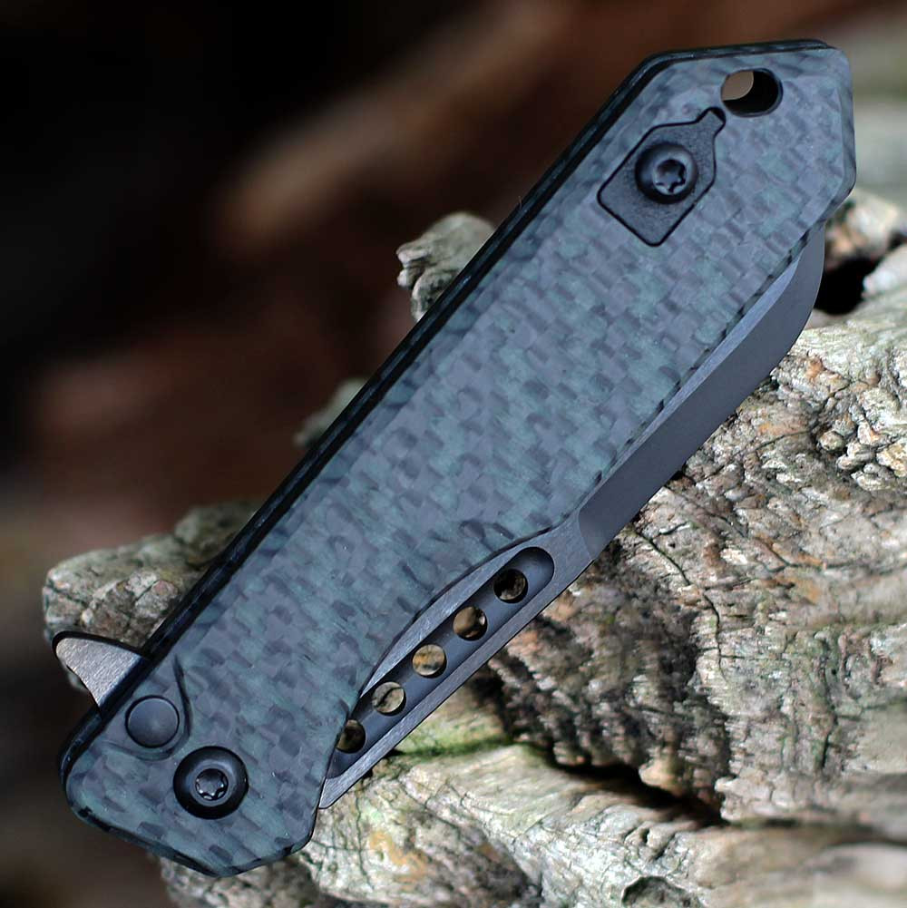 Heretic Knives Jinn Manual H213-6A-GLOCF glow-in-the-dark carbon fiber handle close-up — woven carbon texture, black titanium hardware, finger groove