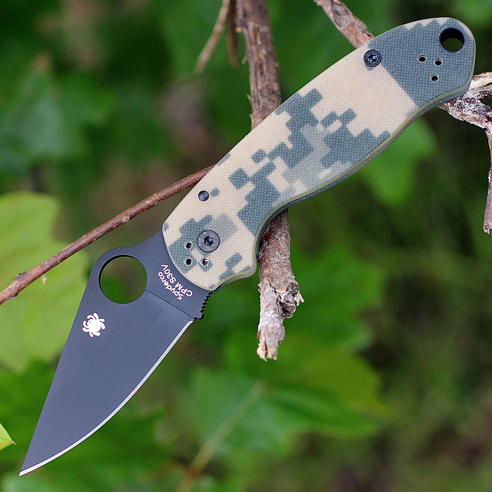 The Spyderco Para 3 C223GPCMOBK is shown open against a white background. The black DLC-coated clip point blade with a Trademark Round Hole extends from a digital camo G-10 handle.