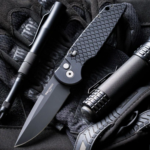 Tactical folding knife with textured black handle beside tactical gear