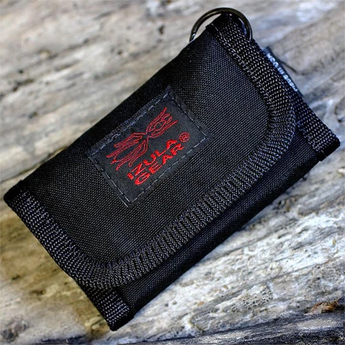 The Izula Gear Wallet E&E Kit (ESEE-WALLET-KIT) shown open as a black Cordura tri-fold with its mini titanium blade, ferro/magnesium rod, ESEE AH-1 Arrowhead, button compass, signal mirror, Kevlar cordage, fish hooks, magnets, and E&E reference cards.