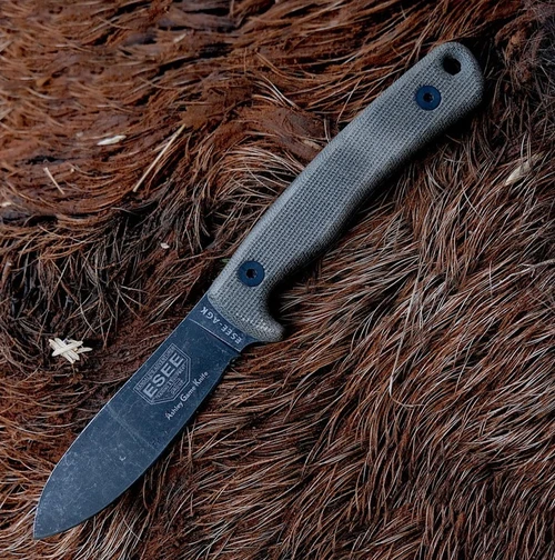 The ESEE Ashley Game Knife (ESEE-AGK) shown with its 3.5-inch 1095 full tang plain edge drop point blade in a black oxide finish and flat grind, gray canvas Micarta handle, and its premium brown leather sheath.