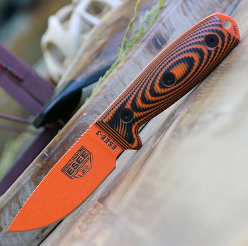 The ESEE-3 3D Handle (ESEE-3PMOR-006) shown with its 3.875-inch 1095 drop point blade in an orange finish and flat grind, 3D black/orange G-10 handle scales, and its injection-molded black polymer sheath.