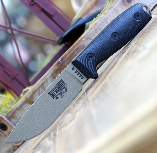The ESEE-4 3D Handle (ESEE-4PDE-001) shown with its 4.50-inch 1095 drop point blade in a Dark Earth finish and tall flat grind, 3D black G-10 handle scales, and its injection-molded black polymer sheath.