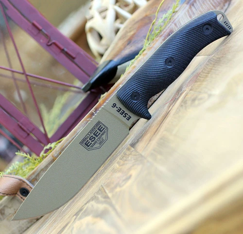 The ESEE-6 3D Handle (6PDE-001) shown with its 6.50-inch 1095 plain edge drop point blade in a Dark Earth finish and flat grind, 3D black G-10 handle scales with finger choil, and its injection-molded black plastic sheath.
