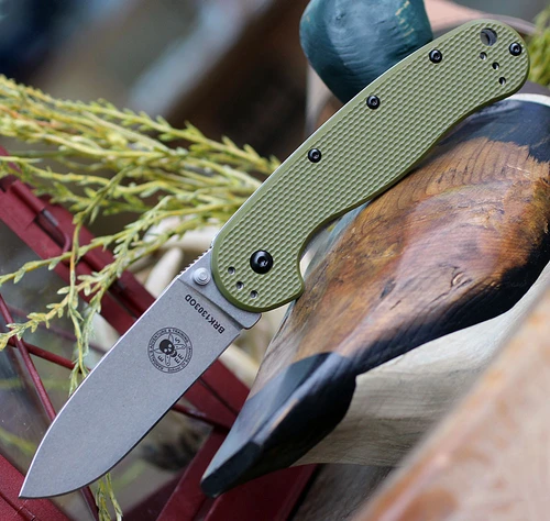 The ESEE Avispa (BRK1303OD) shown with its 3.50-inch SK-5 drop point blade in a stonewash finish and flat grind, modeled after the Laser Strike fixed blade, textured OD Green polymer handle scale with stainless steel frame lock, and pocket clip for tip-up or tip-down carry.