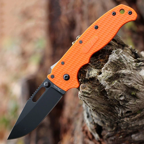 The Demko AD20.5 Shark Lock open, showing its 3.25-inch black-finished, flat-ground AUS-10A clip point blade, orange textured Grivory scales over steel liners, the spine-mounted Shark-Lock fin, a thumb stud and thumb hole, and a tip-up pocket clip.