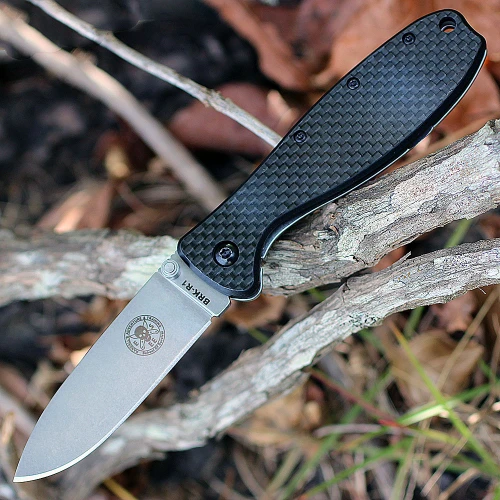 The ESEE Zancudo (BRKR2CF) shown with its 2.94-inch D2 drop point blade in a stonewash finish and flat grind, black carbon fiber and G-10 handle with steel frame lock, and reversible pocket clip for tip-up or tip-down carry.