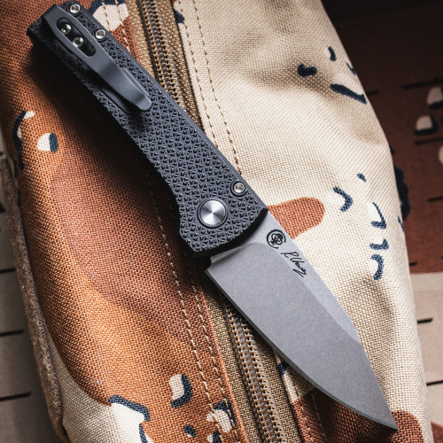 Pro-Tech Chaves Scapegoat Compact BSA26.Scapegoat.1 shown open at an elevated angle on the desert camouflage bag background. This view displays the spine and handle profile of the deployed knife, with the black carbide-textured aluminum scales and the Scapegoat Compact's overall proportions clearly visible.