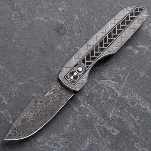 Pro-Tech VERO Synapse 2 Custom 002 shown open on a gray slate surface. The Chad Nichols Raindrop Damascus blade is fully deployed and the full profile of the knife is visible, with the 2-tone blasted and tumbled 17-4 herringbone textured steel handle and deployed Damascus blade both clearly in frame.