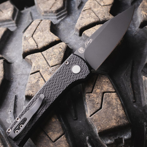 Pro-Tech Scapegoat Compact Auto RCS1106 — open, carbide textured black handle and push button detail, DLC black blade, cracked earth background