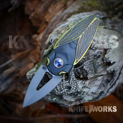 A Rike Cicada-DG folding knife shown with the blade deployed, highlighting the Böhler M390 spear point blade alongside the single-piece dark gray titanium handle and gold finish accents.