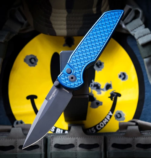 A Pro-Tech TR-3 Integrity manual button-lock folding knife shown with the blade deployed, highlighting the MagnaCut DLC black spear point blade alongside the blue relic-textured aluminum handle and black double thumbstuds.