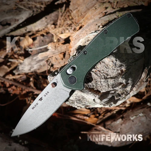 The Buck Range Trail Worn Elite (0791GRS2) shown with its 3.375-inch MagnaCut stonewashed drop point blade in a flat grind, tumbled green aluminum handle scales, and its deep-carry tip-up pocket clip. The crossbar lock mechanism is visible along the spine of this lightweight EDC folder.