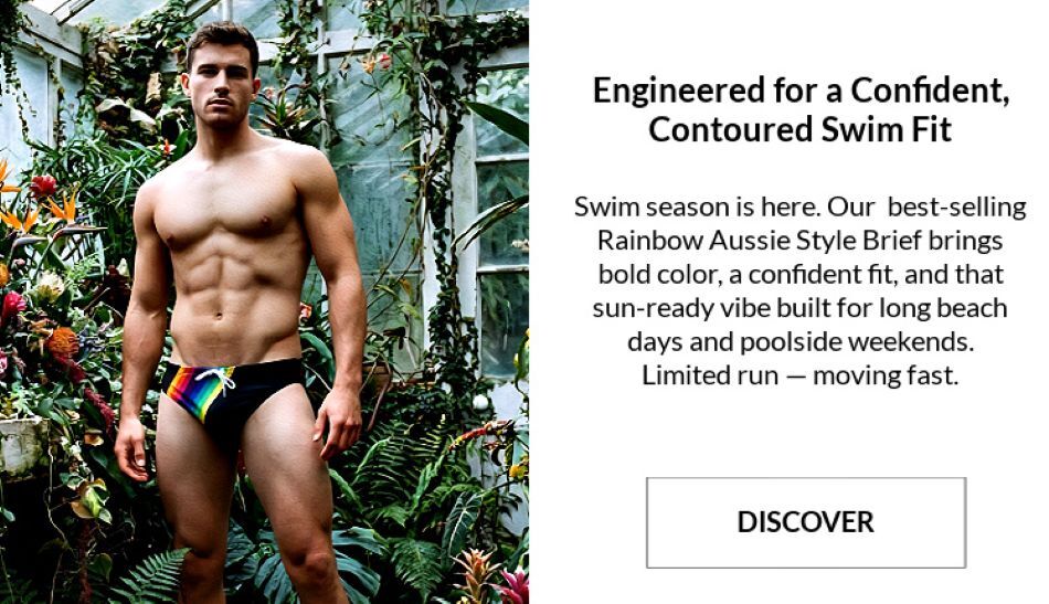Man standing shirtless in an atrium wearing a pair of Jack Adams' Rainbow Swim Briefs