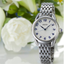 Seiko Ladies SUR561P1 con esfera blanca, números azules y brazalete de acero en composición lifestyle con flores blancas