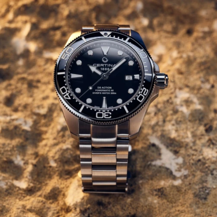Reloj Certina DS Action Diver C032.607.11.051.00 con esfera negra y bisel cerámico sobre superficie de piedra