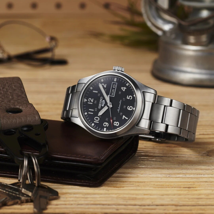 Seiko 5 Sports Field SRPJ81K1 con esfera negra y brazalete de acero sobre superficie de madera