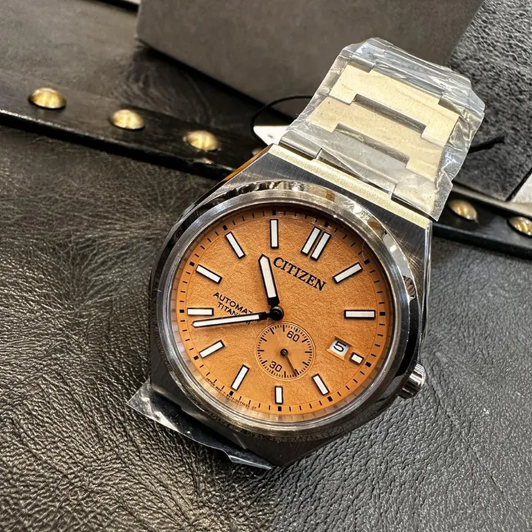 Reloj Citizen Super Titanium NJ0180-80Z con esfera salmón y brazalete de titanio sobre superficie oscura