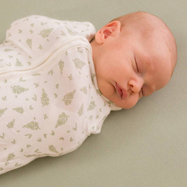 Baby sleeping dressed with arms in a sleep store 0.2 tog organic cotton swaddle bag in little leaves design