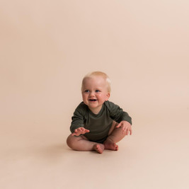 A baby sitting down wearing The Sleep Store All Seasons Merino/Tencel Long Sleeve Bodysuit in the colour Olive.