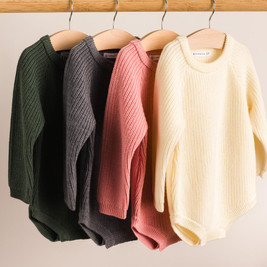 A hanging shot of The Sleep Store Merino Knitwear Bubblesuit in Dark Green, Grey Marl, Pink and Cream on a Wooden rail.
