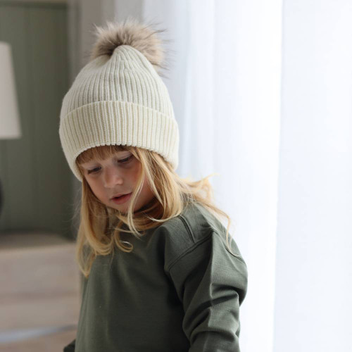 A young girl wearing a Cream colour Sleep Store Knitwear Pompom Beanie.