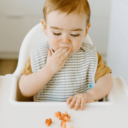 Baby eating in high chair wearing a Little Unicorn Muslin Bib - Grey Stripe.jpg