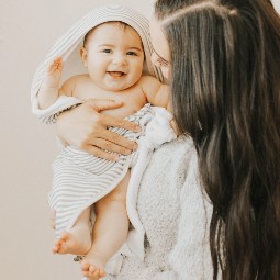 Smiling baby held by mum wrapped in Little Unicorn Hooded Baby Towel - Grey Stripe.jpg