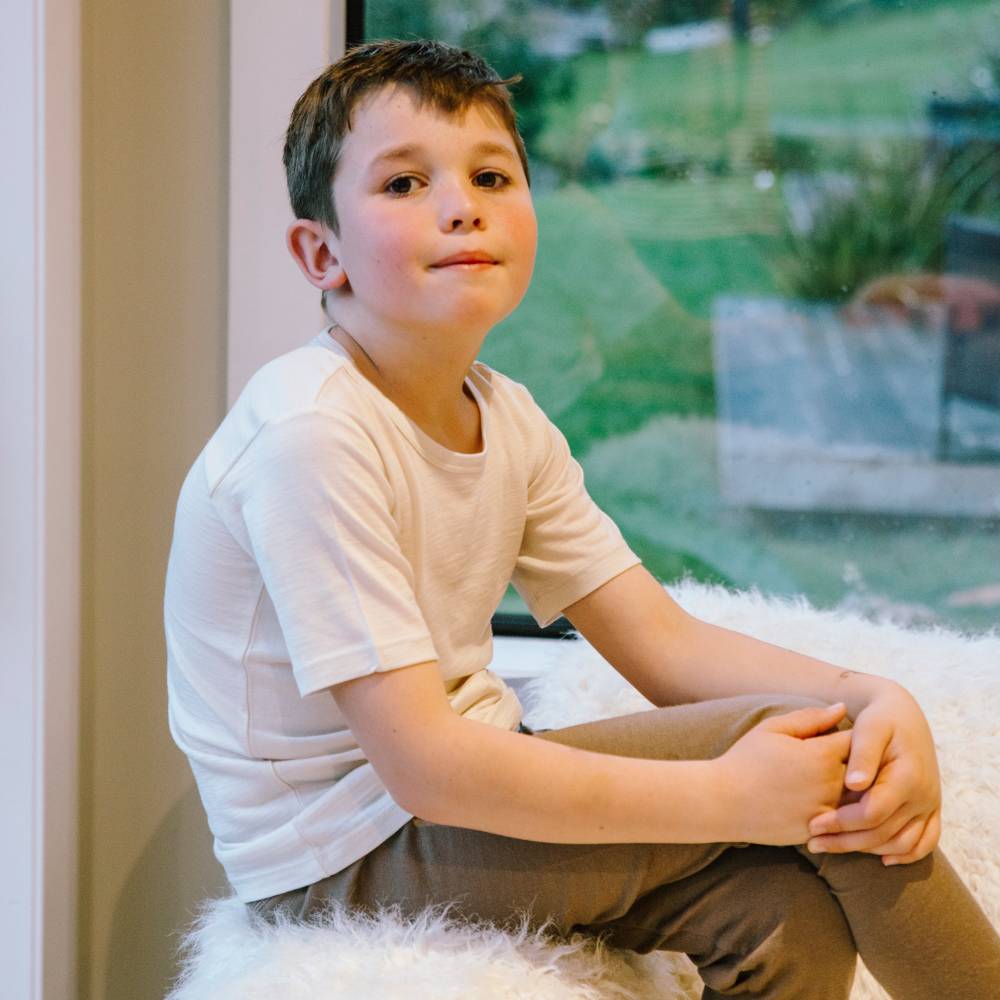 Boy sitting in window wearing The Sleep Store All Seasons Merino/Tencel Kids Short Sleeve Top in Milk