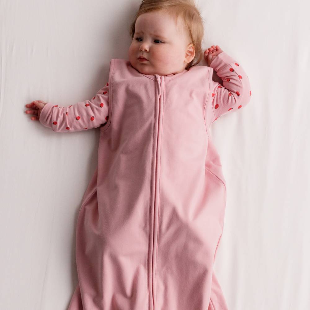 Baby lying awake wearing The Sleep Store Organic Cotton 1.0 tog Sleeping Bag in Blush