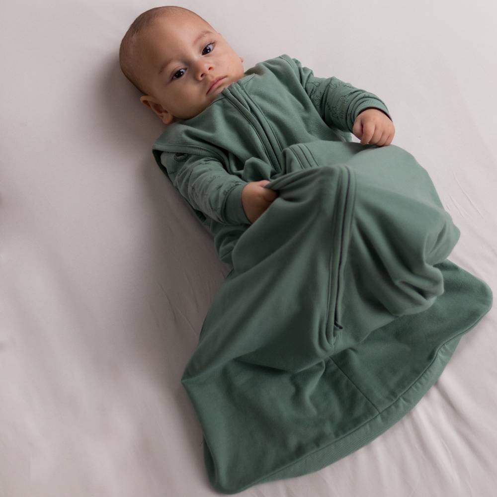 Boy lying awake and kicking up legs wearing The Sleep Store Organic Cotton 1.0 tog Sleeping Bag in Fern