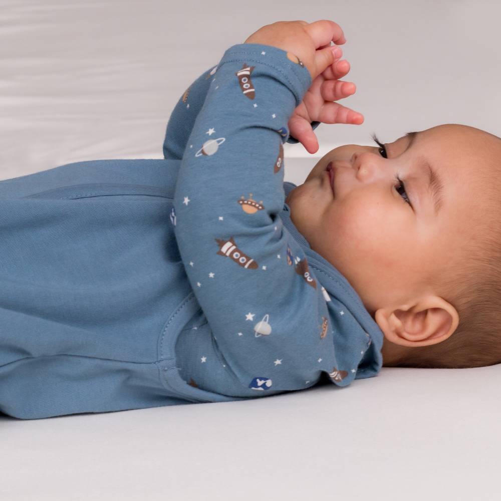 Baby boy looking at hands wearing The Sleep Store Organic Cotton 1.0 tog Sleeping in size 3 - 24 months.