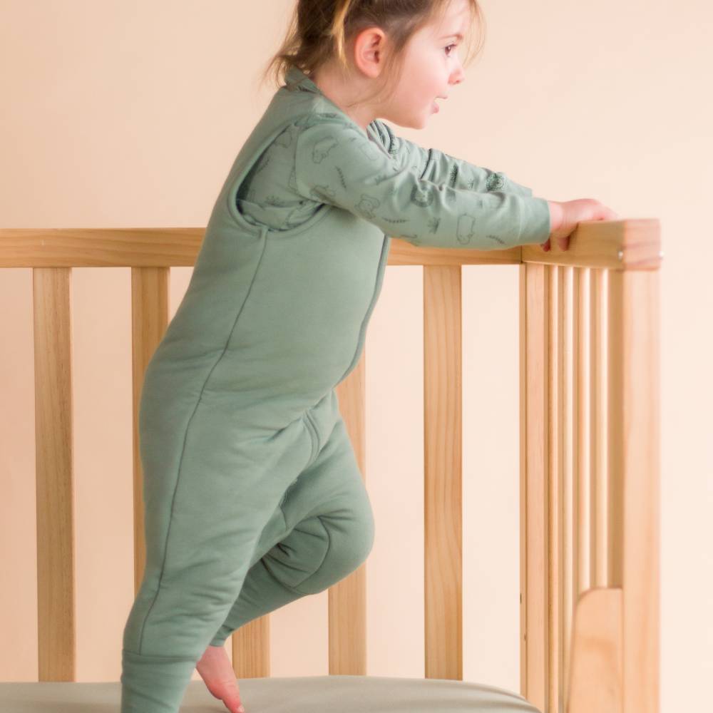 Toddler jumping in cot wearing The Sleep Store Organic Cotton 3.0 tog Sleeping Suit in Fern