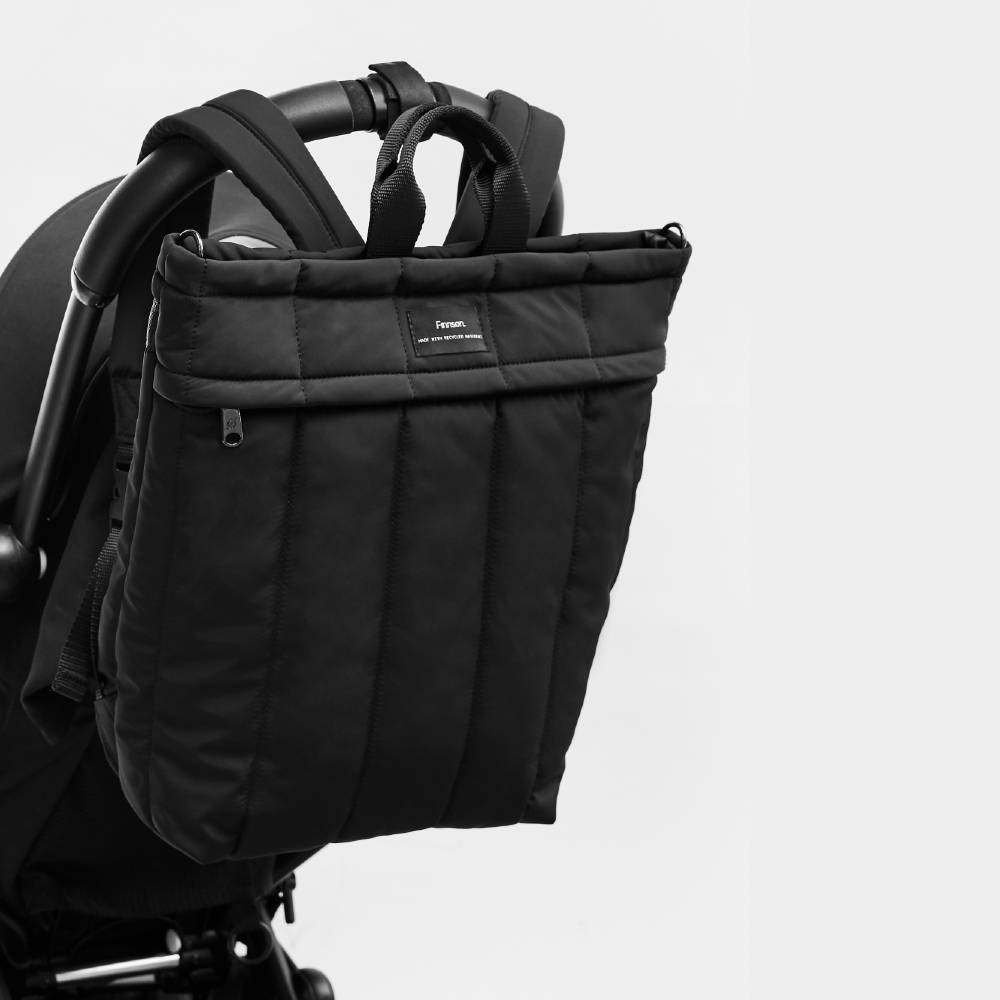 The Finnson RAE eco changing backpack in black hanging from a stroller
