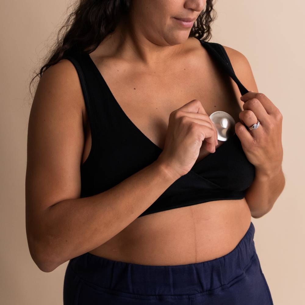 A woman wearing The Sleep Store All Seasons Merino/Tencel Busty Sleep Bra (D+ Cup Sizes) in the colour Black putting a breast in one side of the bra.